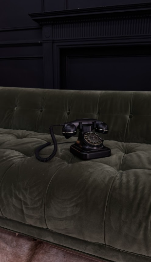 Vintage black rotary telephone resting on a tufted dark green velvet sofa — moody, expensive, unbothered